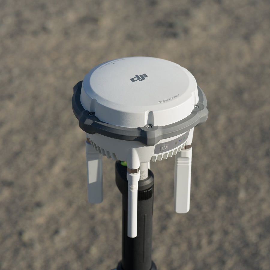 A DJI D-RTK 3 Multifunctional Station set up on a survey tripod outdoors on open ground
