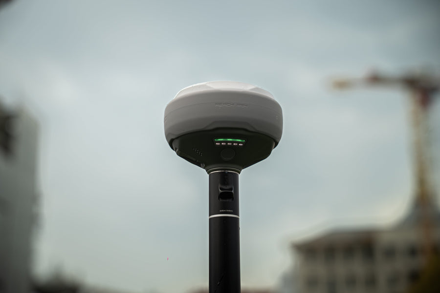 An Emlid Reach RS4 GNSS receiver on a survey pole against a city skyline